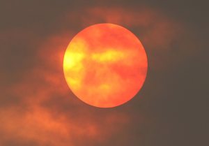 the sun is an orange ball behind the smoke clouds